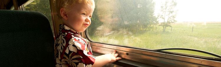 Ett barn står på tågsäte och tittar ut på det gröna landskapet utanför tågfönstret.