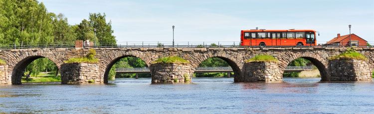 En buss som kör på en gammal stenbro över en kanal