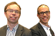 Porträtt av två leende män i glasögon och grå kostym