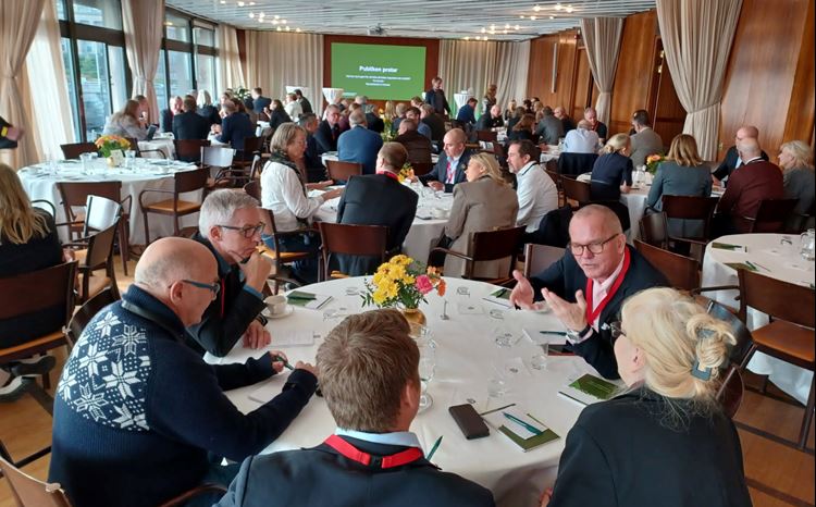 Personer samtalar vid ett antal runda bord i en konferenssal.