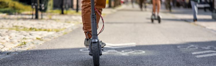 Cykelväg och person som åker på en elsparkcykel, enbart nedre delen av benen och cykeln syns i bild.