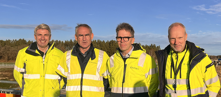 Blå himmel och soligt väder. Fyra män med varseljackor ler mot kameran.