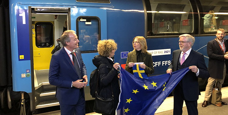 Flera personer står intill ett tåg, några av dem håller upp EU-flaggan och en svensk flagga.