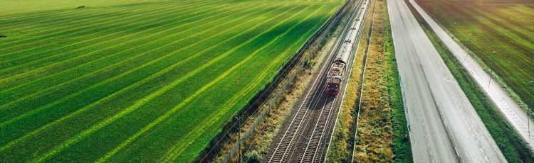 Tåg sveper fram på järnväg mellan ängsmark och väg