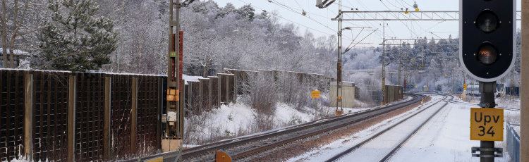 Järnväg med dubbelspår i vinterlandskap, en järnvägssignal i förgrunden.