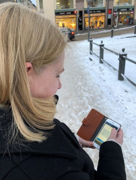 Ung kvinna läser i sin mobil. I bakgrunden syns snöig stadsmiljö.