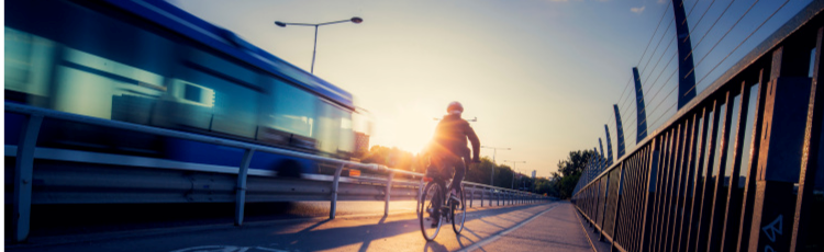 Cyklist i motljus på cykelväg, buss i bakgrunden.