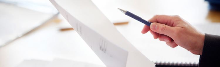 En hand som håller i en penna och ett dokument. 