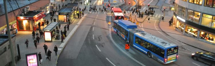 Vy över stadsdel med bussar och människor i rörelse.
