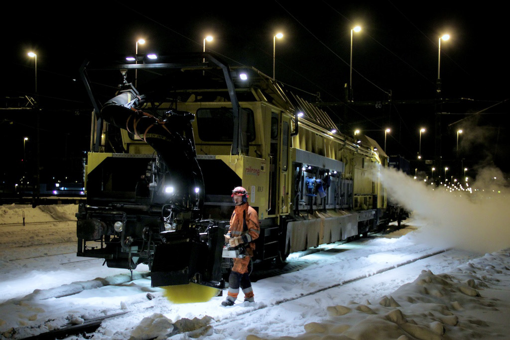 Snöröjningsmaskin i natten röjer snö på järnvägen.