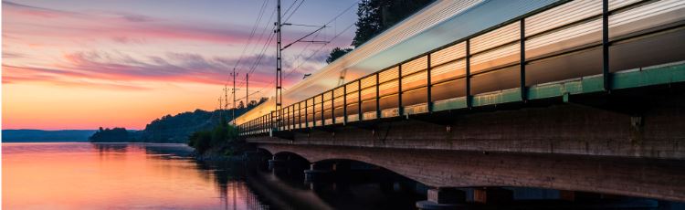 Persontåg på järnväg vid vattren, solnedgång