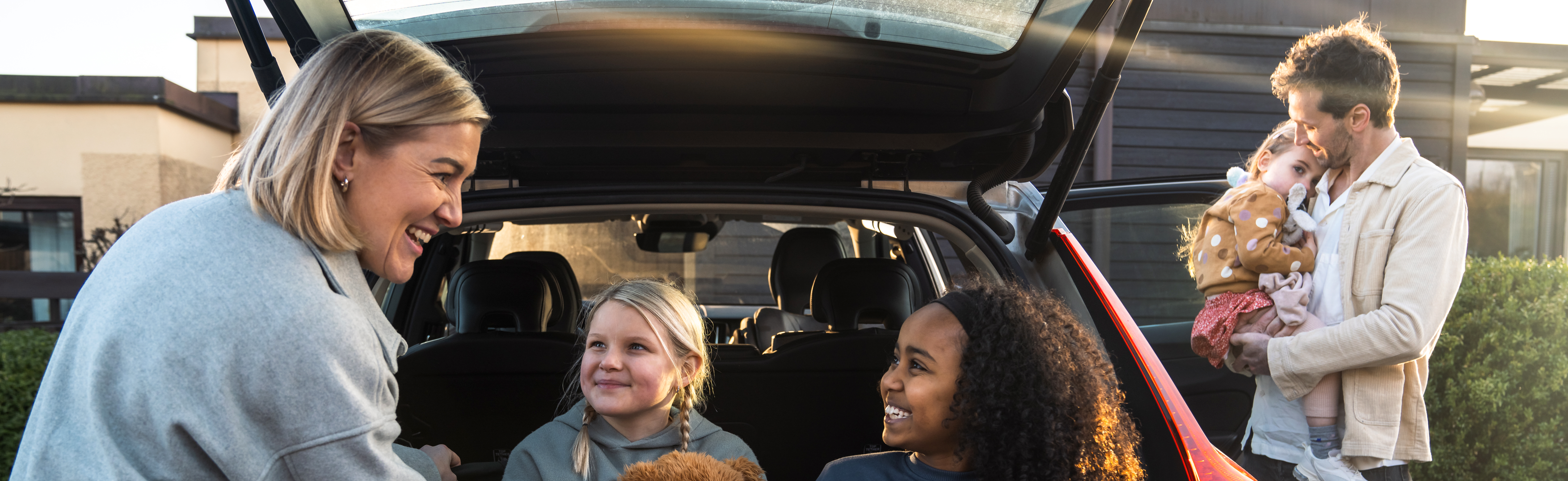 Familj som står vid bil med öppen baklucka och förbereder sig för en bilresa.