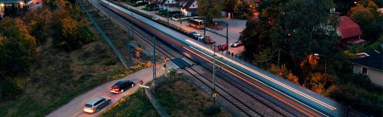 Drönarbild på plankorsning, bilar som väntar på tåget som susar förbi